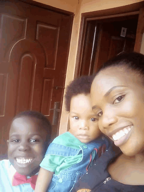a woman is holding a baby and smiling in front of a brown door