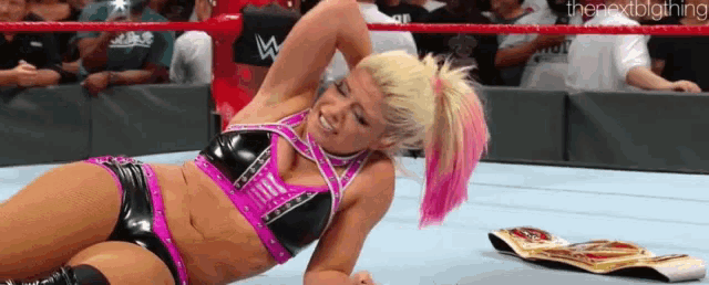 a woman is laying on the ground in a wrestling ring with a championship belt .