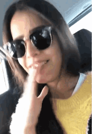 a woman wearing sunglasses is sticking her tongue out while sitting in the back seat of a car .