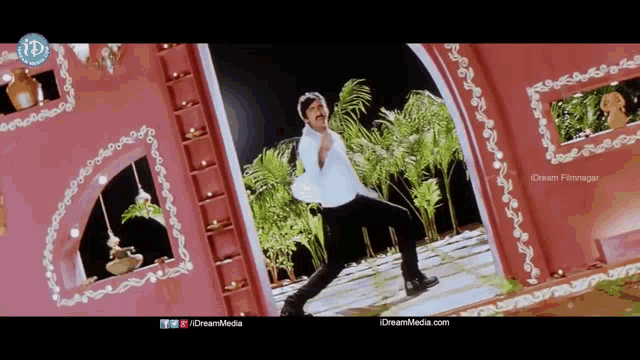 a man in a white shirt is dancing in front of a pink building