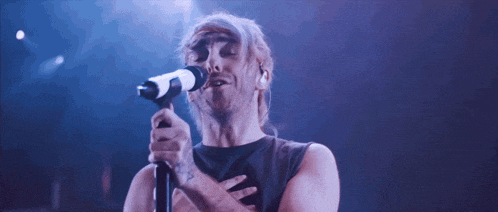 a man singing into a microphone with his hand on his heart