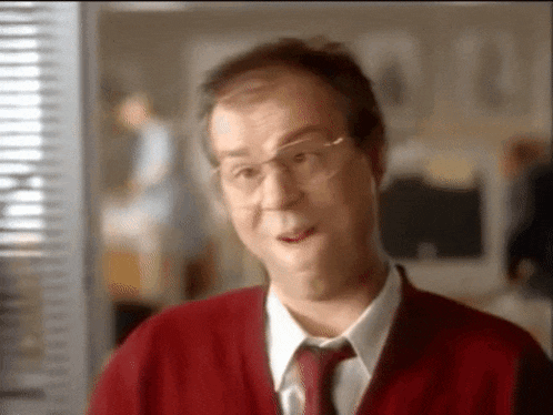 a man with glasses and a red sweater and tie is making a funny face .