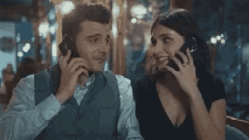 a man and a woman are sitting next to each other talking on their phones .