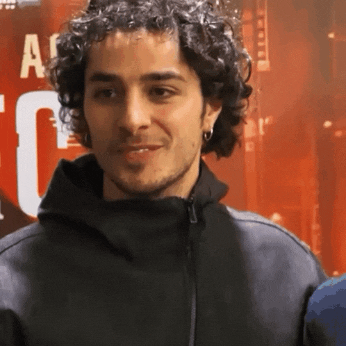 a man with curly hair is smiling in front of a sign that says a