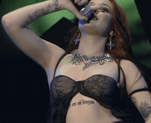 a woman is singing into a microphone and has a tattoo on her chest that says en mi lengua