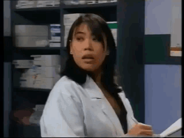 a woman in a white lab coat is standing in front of a shelf in a store .