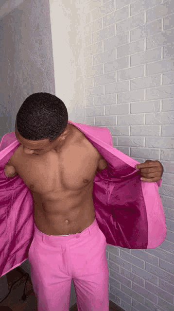 a shirtless man in a pink suit is standing in front of a brick wall