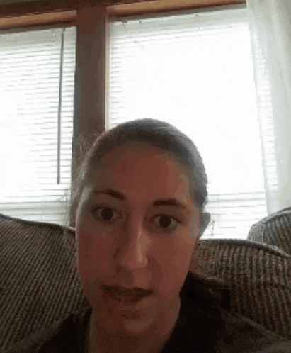 a woman is sitting on a couch in front of a window with blinds on it .