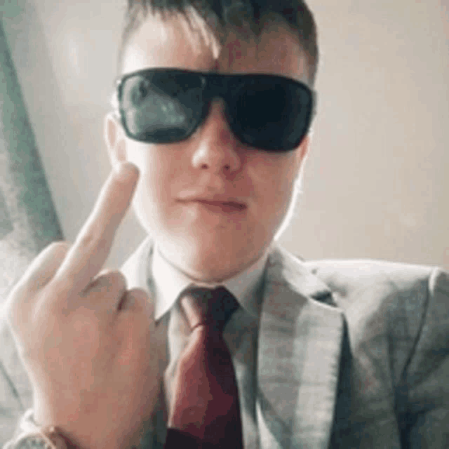 a man in a suit and tie wearing sunglasses giving the middle finger