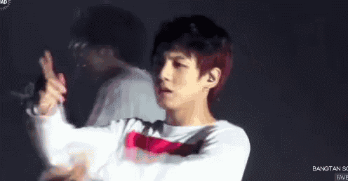 a young man in a white shirt is holding a microphone and making a gesture .
