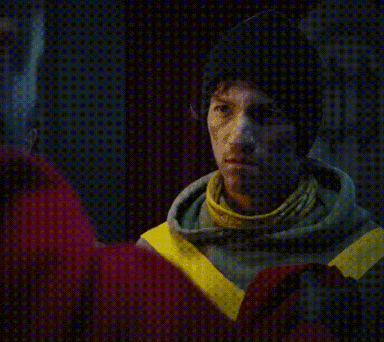 a man wearing a hoodie with yellow stripes on the sleeves looks at the camera