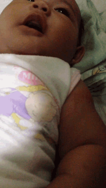 a baby is laying on a bed wearing a sleeveless shirt with a cartoon character on the front