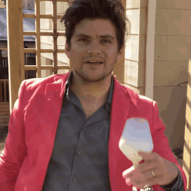 a man wearing a pink jacket is holding a wine glass