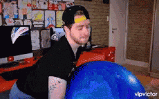 a man in a black shirt is sitting on a blue exercise ball in a room ..