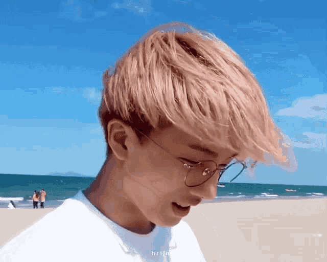a young man wearing glasses is standing on the beach .
