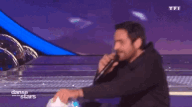 a man is singing into a microphone on a stage in front of a tfi logo