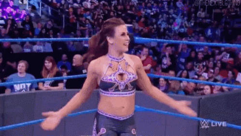 a female wrestler is standing in a wrestling ring with her arms outstretched in front of a crowd .