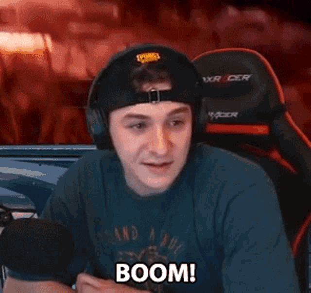 a man wearing headphones and a hat is sitting in front of a microphone and says boom .