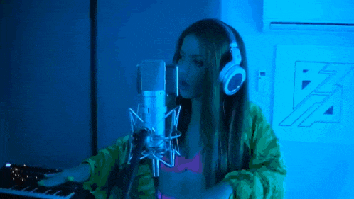 a woman wearing headphones is singing into a microphone while playing a keyboard .
