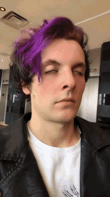 a man with purple hair has his eyes closed and is wearing a black jacket