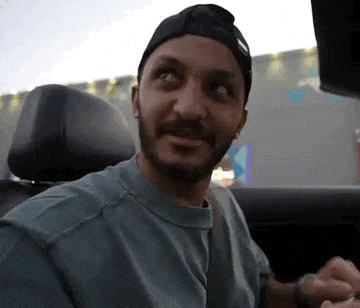 a man with a beard is sitting in the back seat of a car looking at the camera .