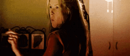 a woman with long hair is standing in front of a mirror in a bedroom .
