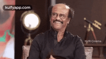 a bald man with glasses and a mustache is sitting in a chair .