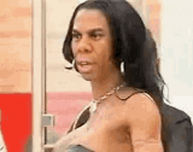 a woman without a shirt is standing in front of a window and making a funny face .