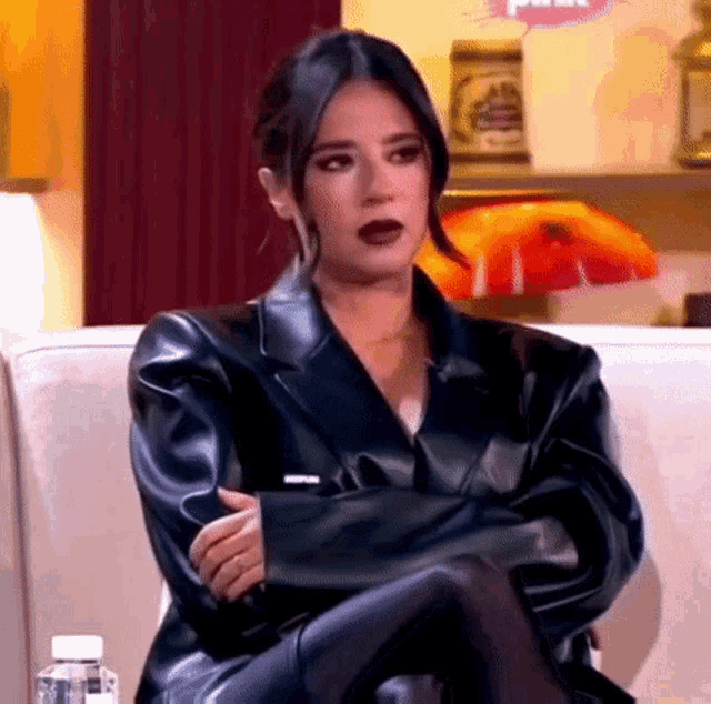 a woman in a black leather jacket is sitting on a couch with her legs crossed .