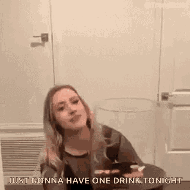 a woman is sitting at a table holding a glass of wine and saying `` just gonna have one drink tonight `` .