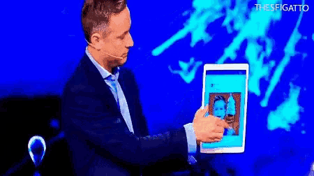 a man in a suit is holding a tablet with a picture of two men on it