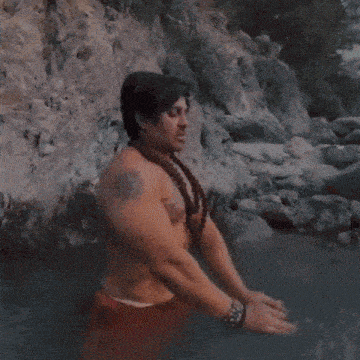 a shirtless man with a tattoo on his chest stands in a body of water