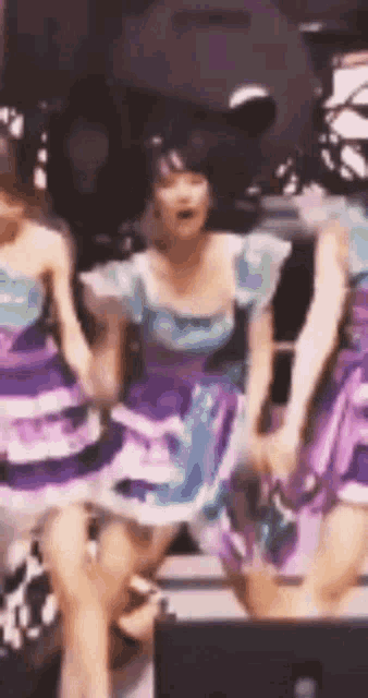 a group of girls in purple and blue dresses are dancing on stage .