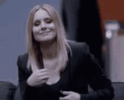 a woman in a black jacket and black top is smiling and holding her chest .
