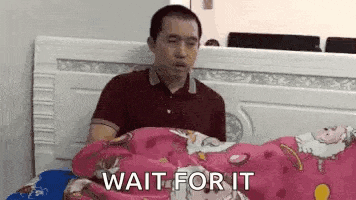 a man is laying on a bed with a pink blanket and the words `` wait for it '' written on the blanket .
