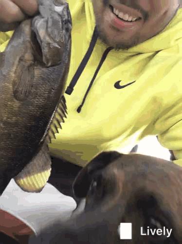a man in a yellow nike hoodie holds a fish