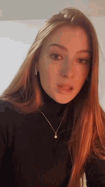 a young woman with long red hair is wearing a black turtleneck and a gold necklace .
