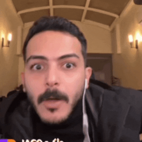 a man with a mustache is wearing earbuds and making a funny face .