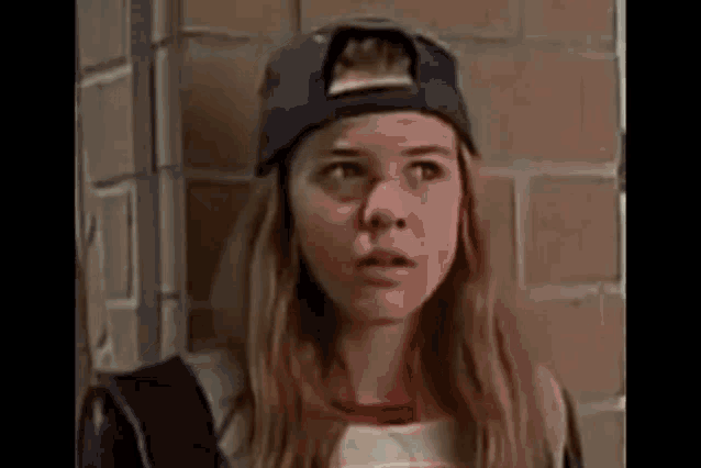 a young woman wearing a baseball cap is standing next to a brick wall .