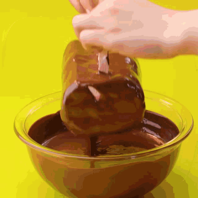 a person dipping a piece of chocolate in a bowl of chocolate