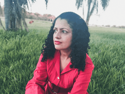 a woman in a red shirt sits on the grass