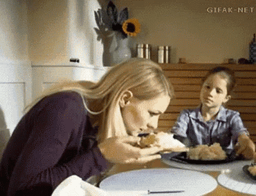 a woman is sitting at a table eating a piece of food while a girl looks on .
