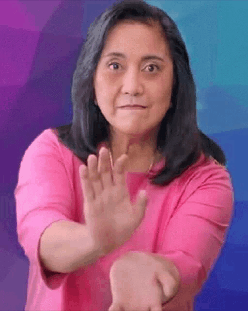 a woman is wearing a pink shirt and making a stop sign with her hands .