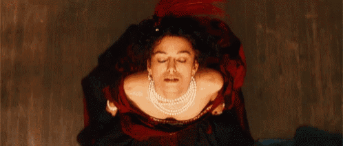 a woman in a red dress and pearls is looking up at the camera .
