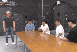 a group of men are sitting around a table and one of them is wearing a black shirt that says ' a ' on it