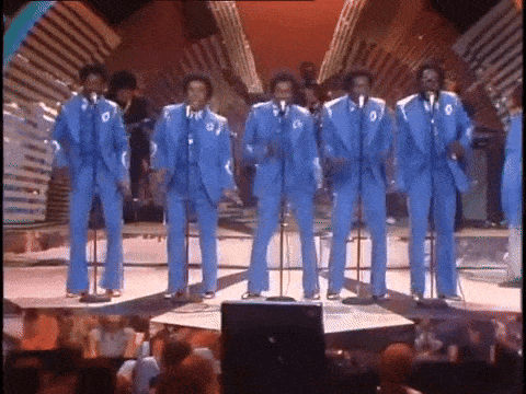 a group of men in blue suits singing into microphones on a stage