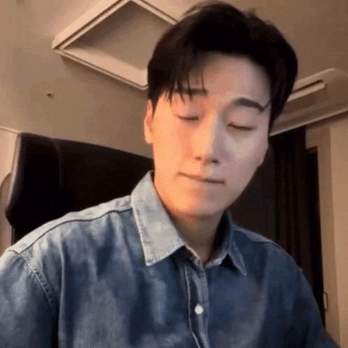 a man in a denim shirt is sitting with his eyes closed