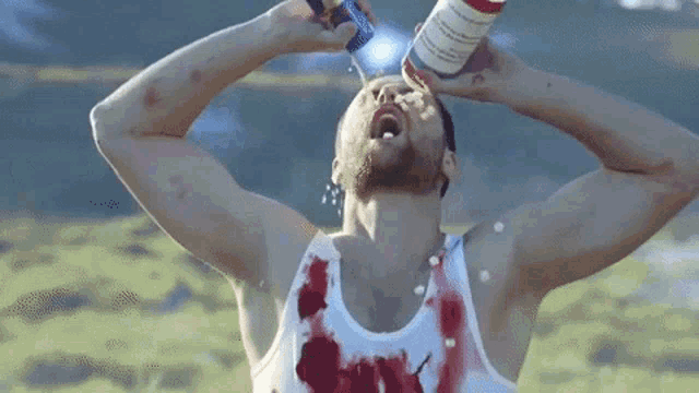 a man in a bloody tank top is drinking from a can of red bull
