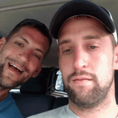 two men are posing for a picture with one wearing a baseball cap