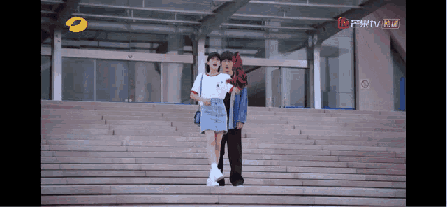 a man and a woman are walking down a set of stairs in front of a building that says tv on the bottom left